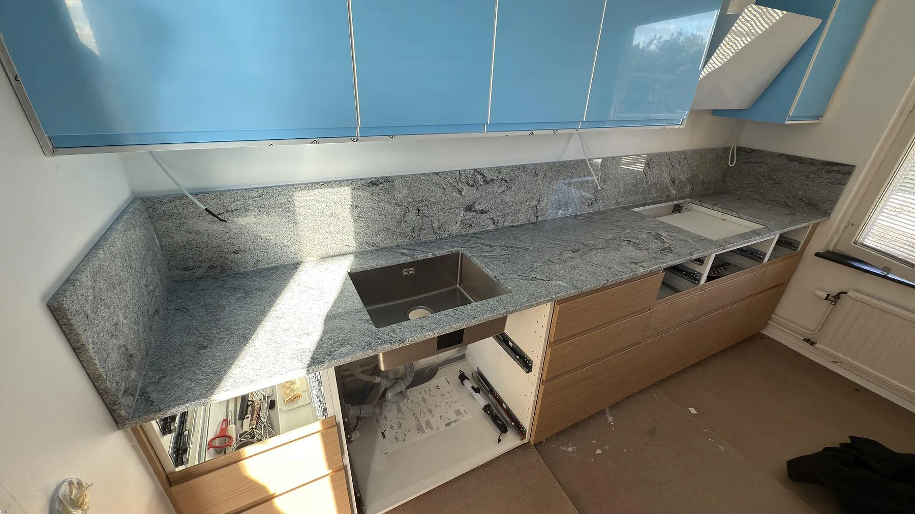 Køkkenbordplade i poleret Viscont White granit med uppvikt stänkkant i ett køkken under montering i Solna.