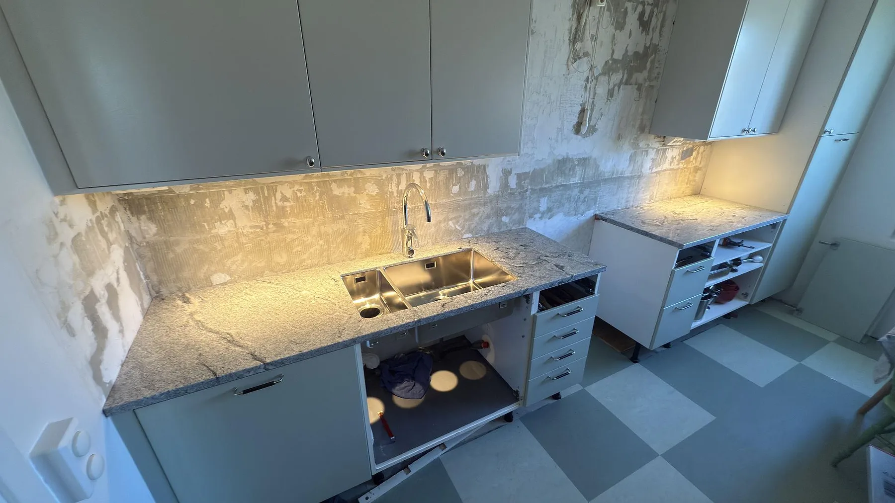 Vinkelställd køkkenbordplade i Viscont White, hvid granit med grå og svarta årer og poleret overflade, med underlimmad rostfri vask og stænkplade i samme sten, fotograferad under montering i ett køkken i Solna.